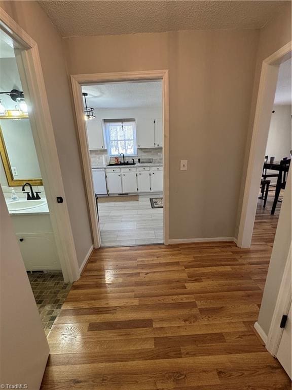 hall featuring a sink, a textured ceiling, baseboards, and wood finished floors