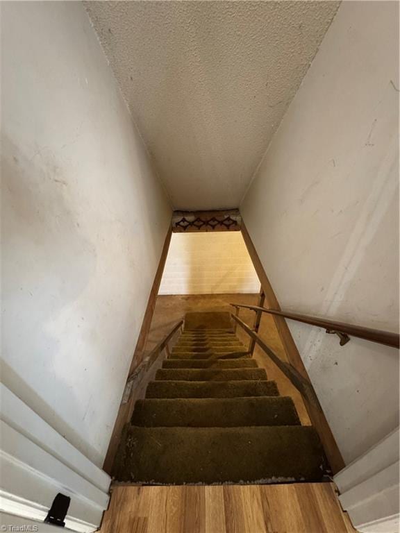 stairway with a textured ceiling and wood finished floors