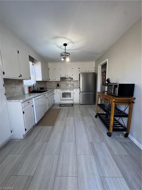 kitchen featuring pendant lighting, sink, white appliances, white cabinets, and decorative backsplash