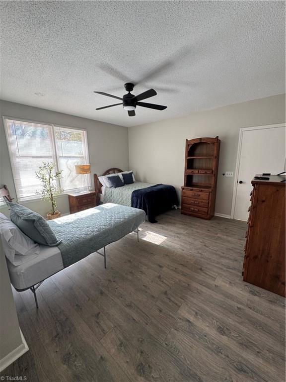 bedroom featuring dark wood-style floors, a textured ceiling, a ceiling fan, and baseboards