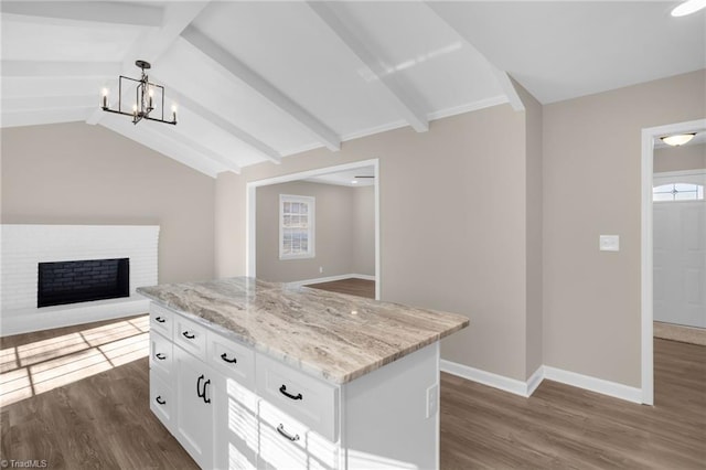 kitchen with a brick fireplace, lofted ceiling with beams, white cabinets, a center island, and hanging light fixtures