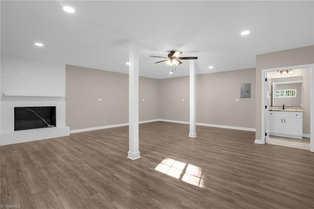 basement featuring ceiling fan, dark wood-type flooring, electric panel, and a brick fireplace