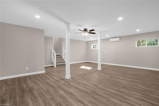 basement featuring dark hardwood / wood-style floors, a healthy amount of sunlight, an AC wall unit, and ceiling fan