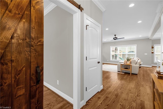 corridor with ornamental molding, a barn door, and hardwood / wood-style floors