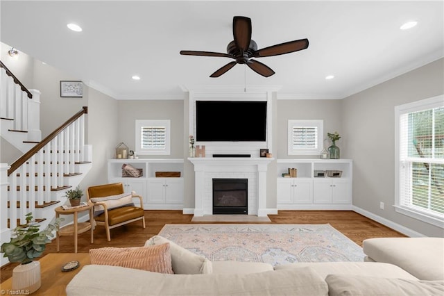 living room with a fireplace, light hardwood / wood-style flooring, ornamental molding, and ceiling fan