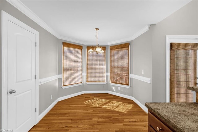 unfurnished dining area featuring crown molding, baseboards, a chandelier, and wood finished floors