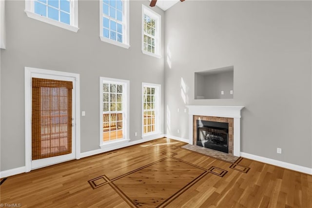 unfurnished living room with a high ceiling, a tile fireplace, baseboards, and wood finished floors