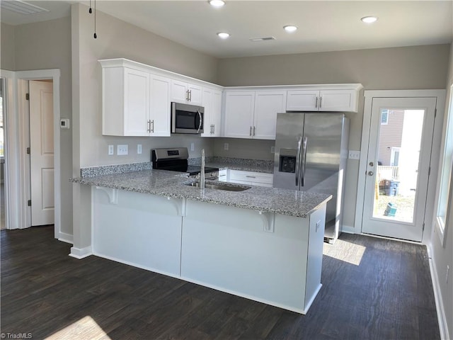 kitchen featuring stainless steel appliances, dark wood-type flooring, white cabinets, light stone countertops, and a peninsula