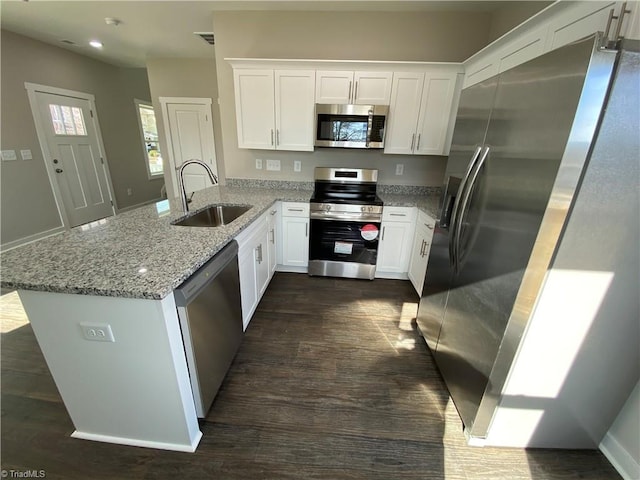 kitchen with a peninsula, white cabinets, stainless steel appliances, and a sink