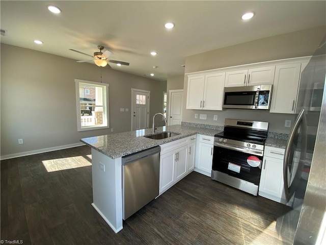 kitchen featuring dark wood-style flooring, stainless steel appliances, white cabinets, a sink, and a peninsula