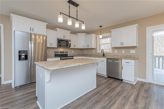 kitchen featuring a sink, a kitchen island, white cabinetry, hanging light fixtures, and appliances with stainless steel finishes