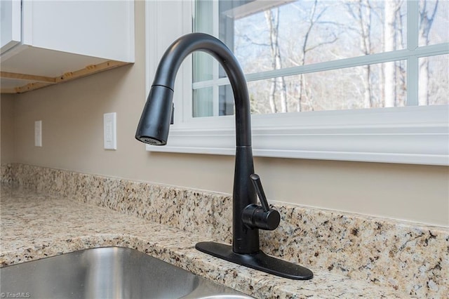 interior details with light stone counters, white cabinetry, and a sink