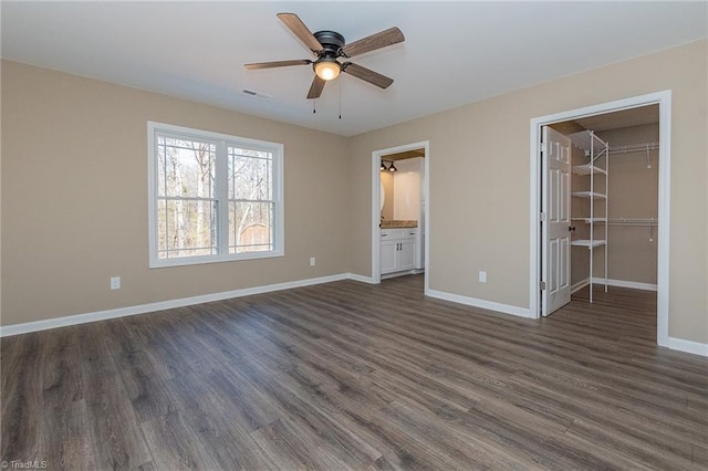 unfurnished bedroom with visible vents, baseboards, a closet, dark wood-style floors, and a walk in closet