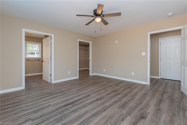 unfurnished bedroom with dark wood-type flooring, a closet, a spacious closet, and baseboards