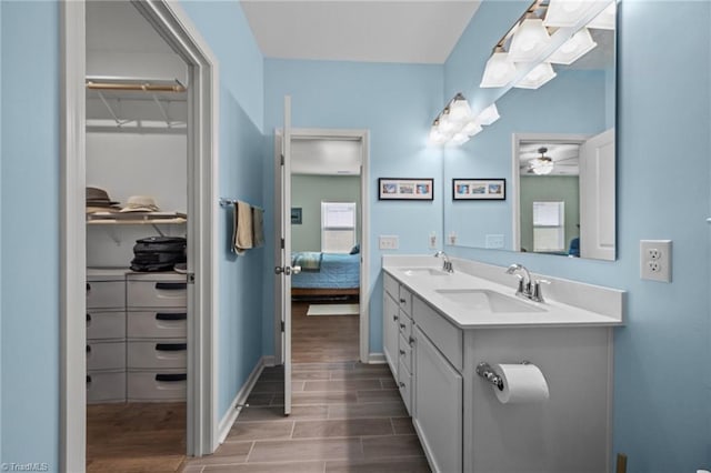 ensuite bathroom with wood finished floors, double vanity, ceiling fan, baseboards, and a walk in closet