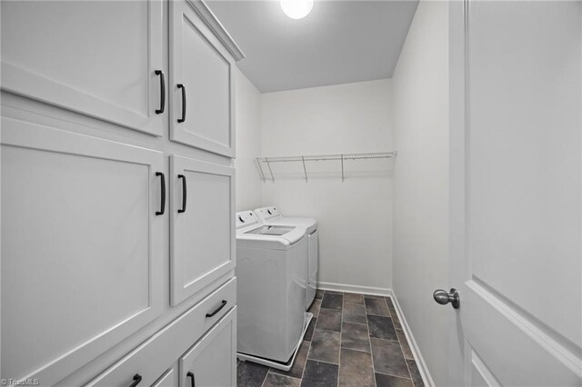 clothes washing area with independent washer and dryer, stone finish flooring, cabinet space, and baseboards