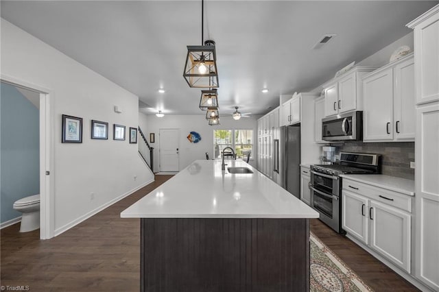 kitchen with appliances with stainless steel finishes, a sink, light countertops, white cabinets, and a kitchen island with sink