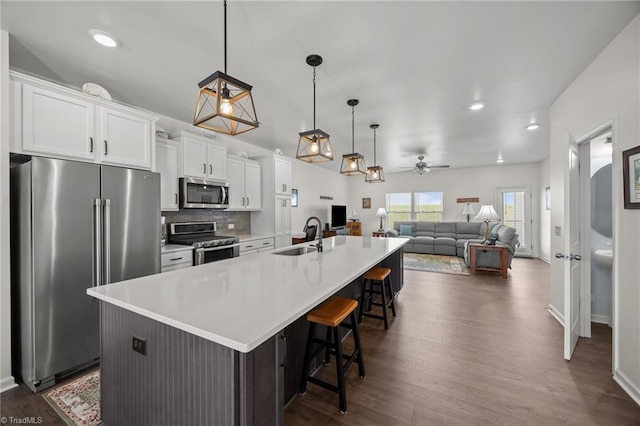 kitchen with appliances with stainless steel finishes, white cabinets, a large island with sink, a kitchen breakfast bar, and light countertops