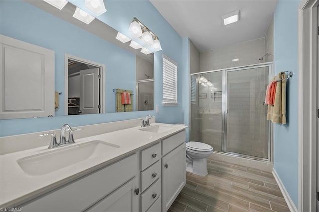 bathroom with a shower stall, wood finish floors, double vanity, toilet, and baseboards