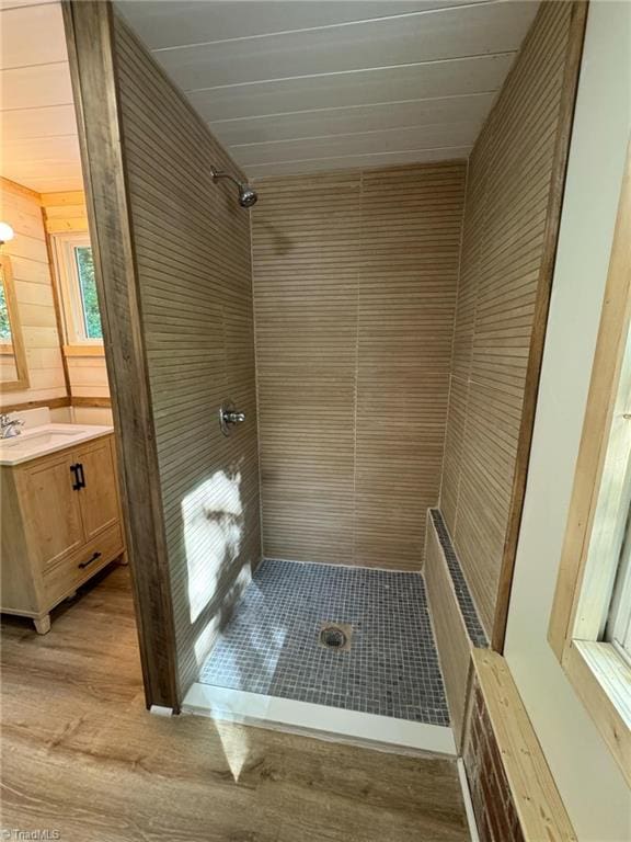 bathroom featuring vanity, wood walls, hardwood / wood-style flooring, and tiled shower