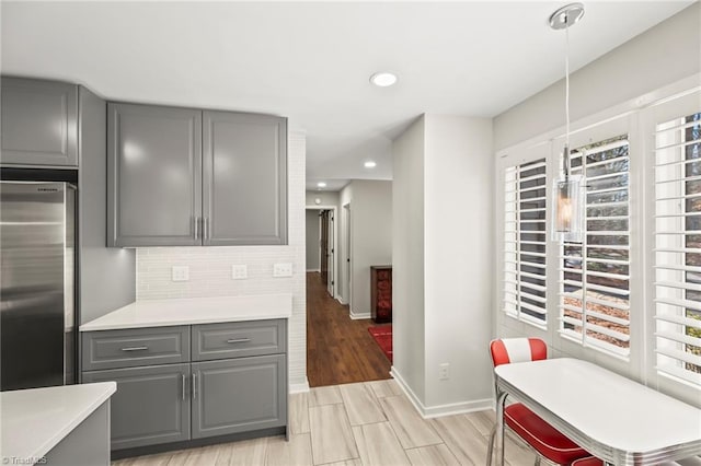 kitchen with stainless steel refrigerator, backsplash, gray cabinetry, and light countertops