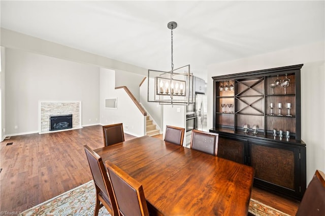 dining room with baseboards, stairs, a stone fireplace, wood finished floors, and a notable chandelier