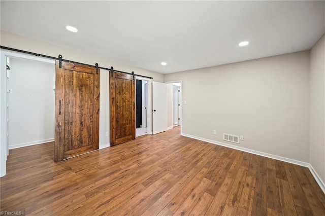 unfurnished bedroom with visible vents, baseboards, a barn door, and hardwood / wood-style floors