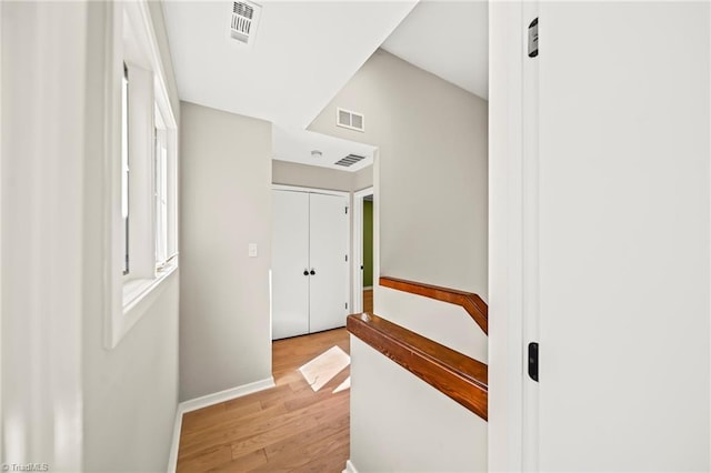 hall with light wood-style flooring, baseboards, and visible vents