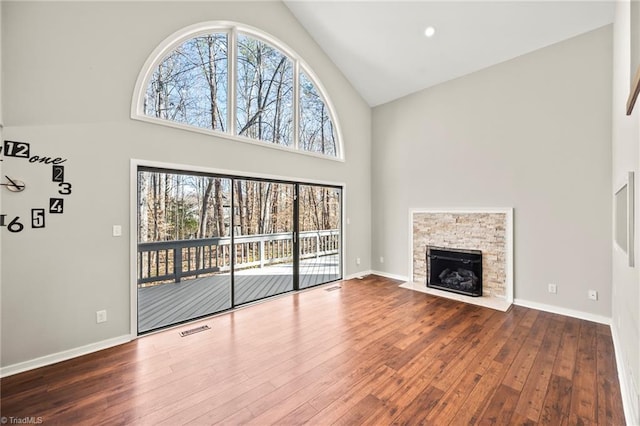 unfurnished living room with visible vents, baseboards, a fireplace, high vaulted ceiling, and wood-type flooring