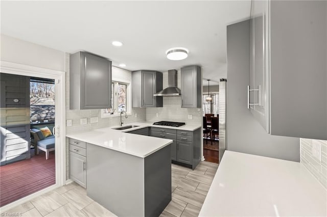 kitchen with black cooktop, a sink, gray cabinetry, wall chimney range hood, and tasteful backsplash