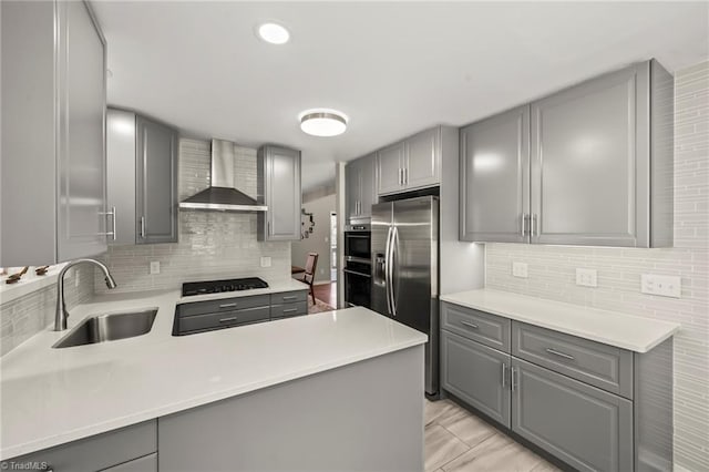 kitchen with gray cabinetry, wall chimney range hood, and a sink