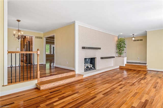 unfurnished living room with ornamental molding, hardwood / wood-style floors, a notable chandelier, and a fireplace