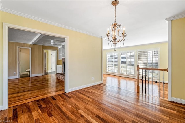 spare room with hardwood / wood-style flooring, crown molding, ceiling fan with notable chandelier, and a fireplace