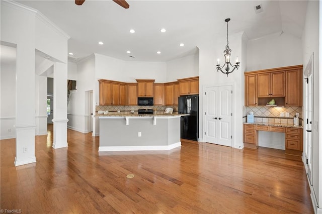 kitchen featuring brown cabinets, a breakfast bar area, decorative backsplash, a towering ceiling, and black appliances