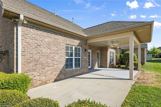 rear view of property featuring roof with shingles, brick siding, ceiling fan, concrete driveway, and a patio area