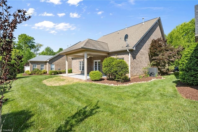 rear view of property with a lawn, a patio, central AC unit, and brick siding