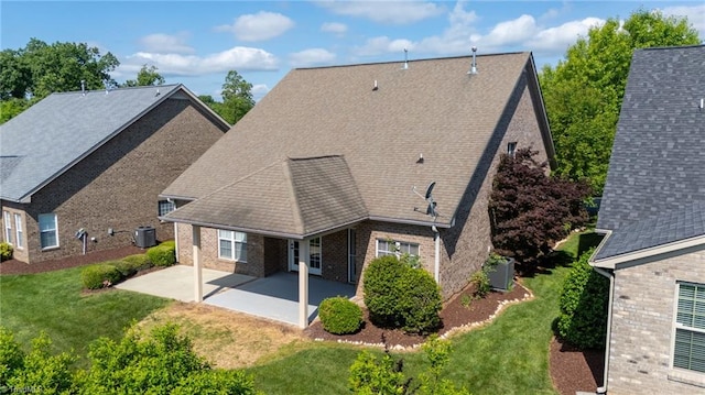 rear view of property with a shingled roof, brick siding, central AC unit, a lawn, and a patio