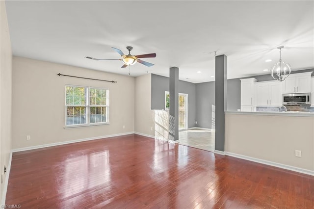 unfurnished living room with ceiling fan with notable chandelier and hardwood / wood-style flooring