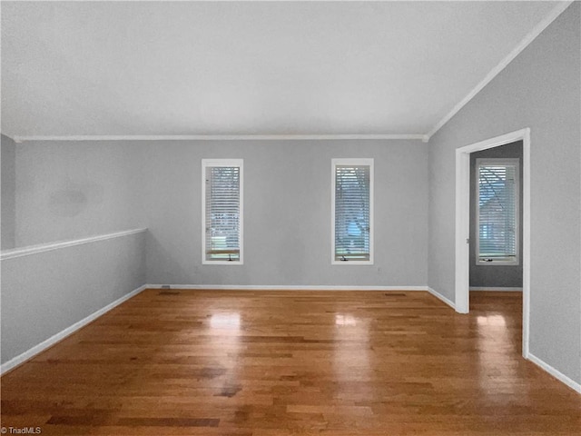 empty room featuring baseboards, lofted ceiling, wood finished floors, and crown molding