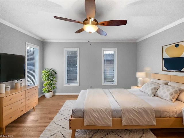 bedroom featuring multiple windows, a ceiling fan, crown molding, light wood finished floors, and baseboards