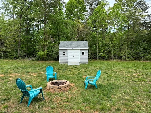 view of yard featuring a wooded view, a fire pit, a storage unit, and an outdoor structure