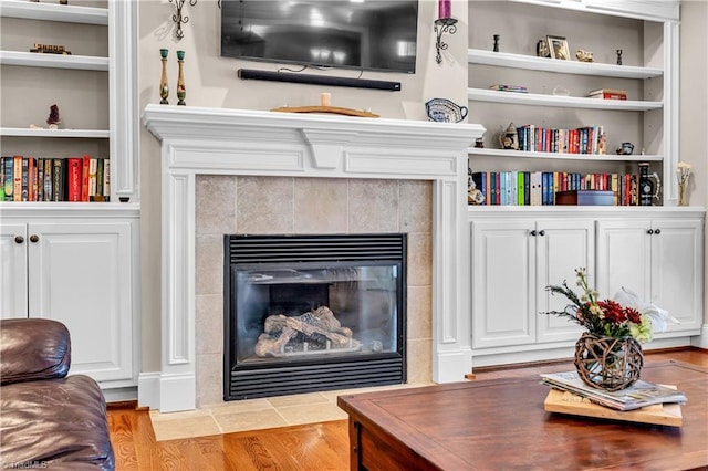 living room featuring built in shelves, light hardwood / wood-style flooring, and a tiled fireplace