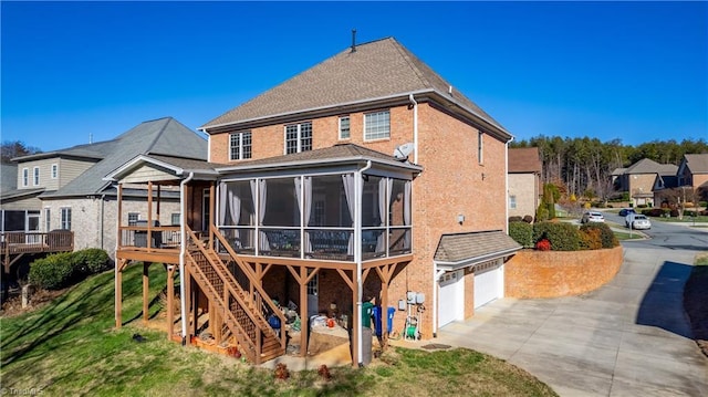 rear view of property featuring a lawn, a sunroom, and a garage