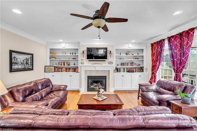 living room with built in shelves, ceiling fan, crown molding, and light hardwood / wood-style flooring