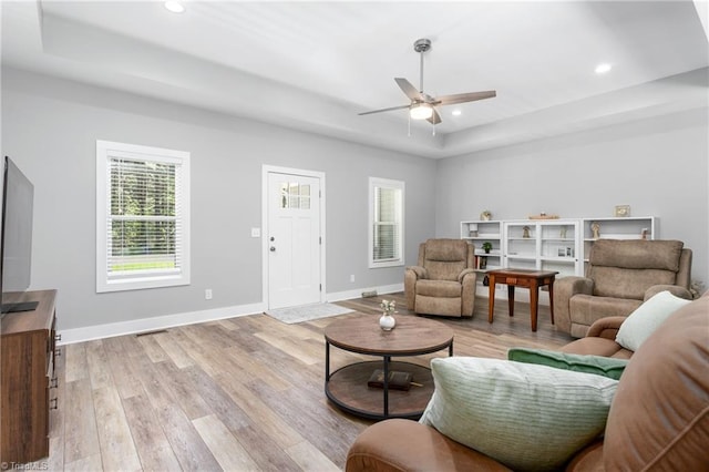 living room with light wood finished floors, ceiling fan, and a tray ceiling