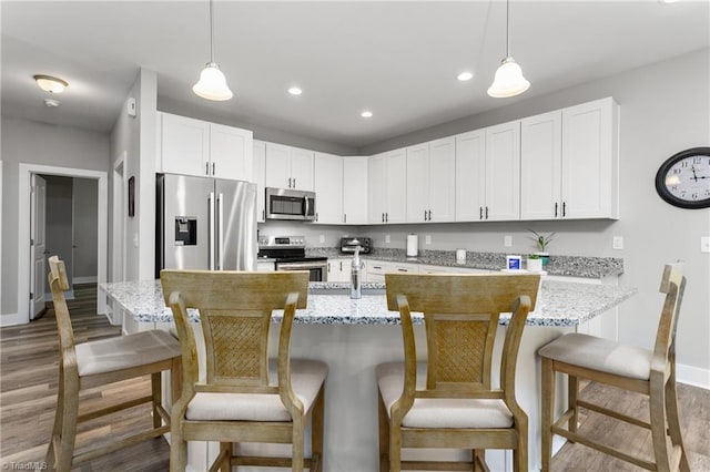 kitchen with hanging light fixtures, stainless steel appliances, wood finished floors, and white cabinets
