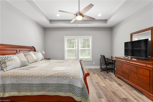 bedroom featuring baseboards, a ceiling fan, light wood finished floors, and a tray ceiling