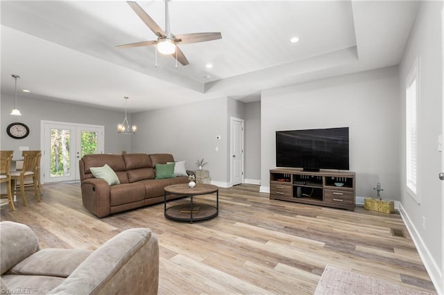 living room featuring baseboards, a raised ceiling, ceiling fan with notable chandelier, and wood finished floors