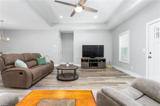 living room with wood finished floors, baseboards, a raised ceiling, ceiling fan with notable chandelier, and recessed lighting
