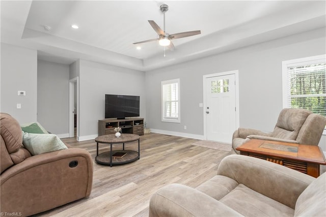 living area with ceiling fan, recessed lighting, baseboards, light wood-type flooring, and a tray ceiling
